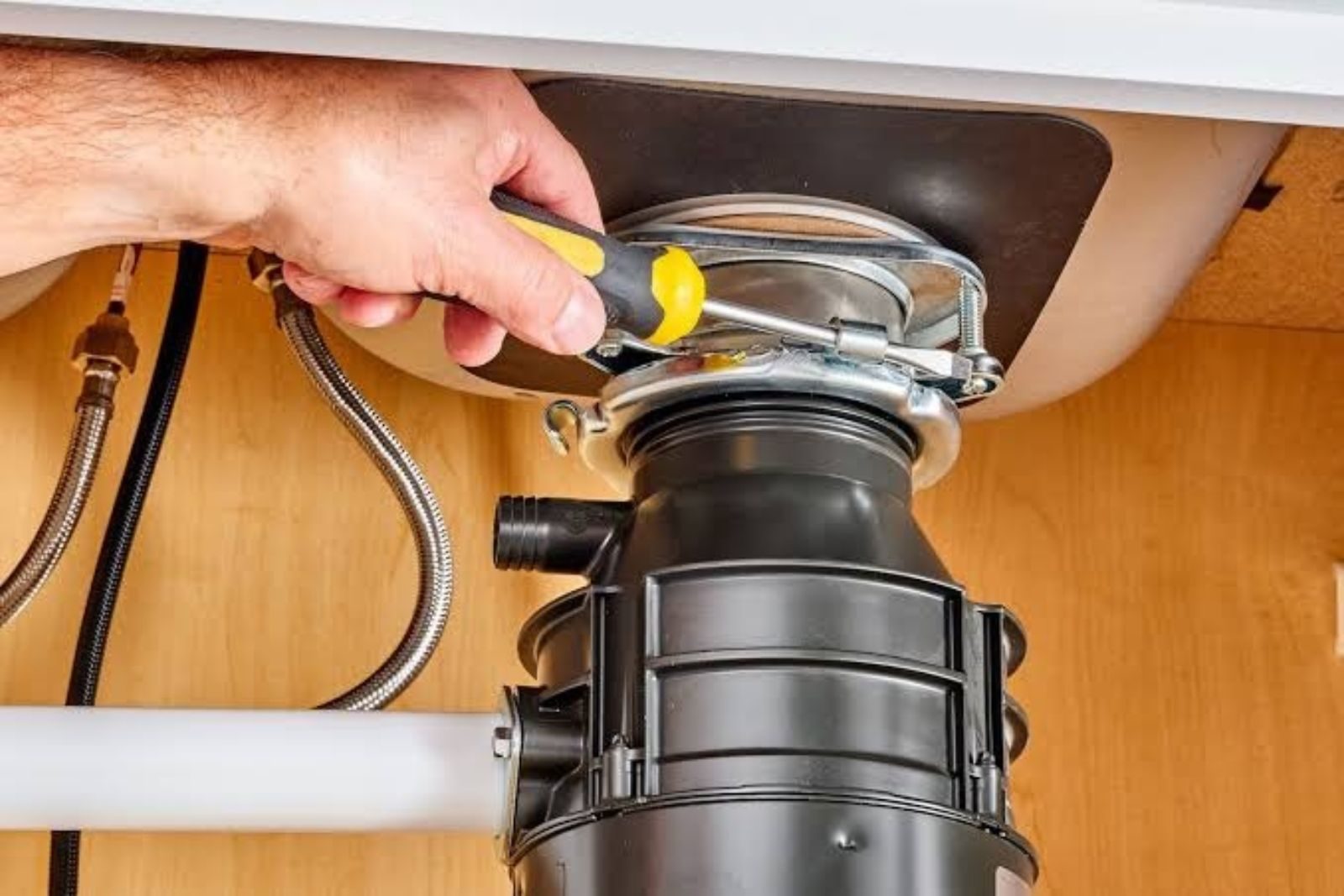 Garbage disposal being repaired under a kitchen sink